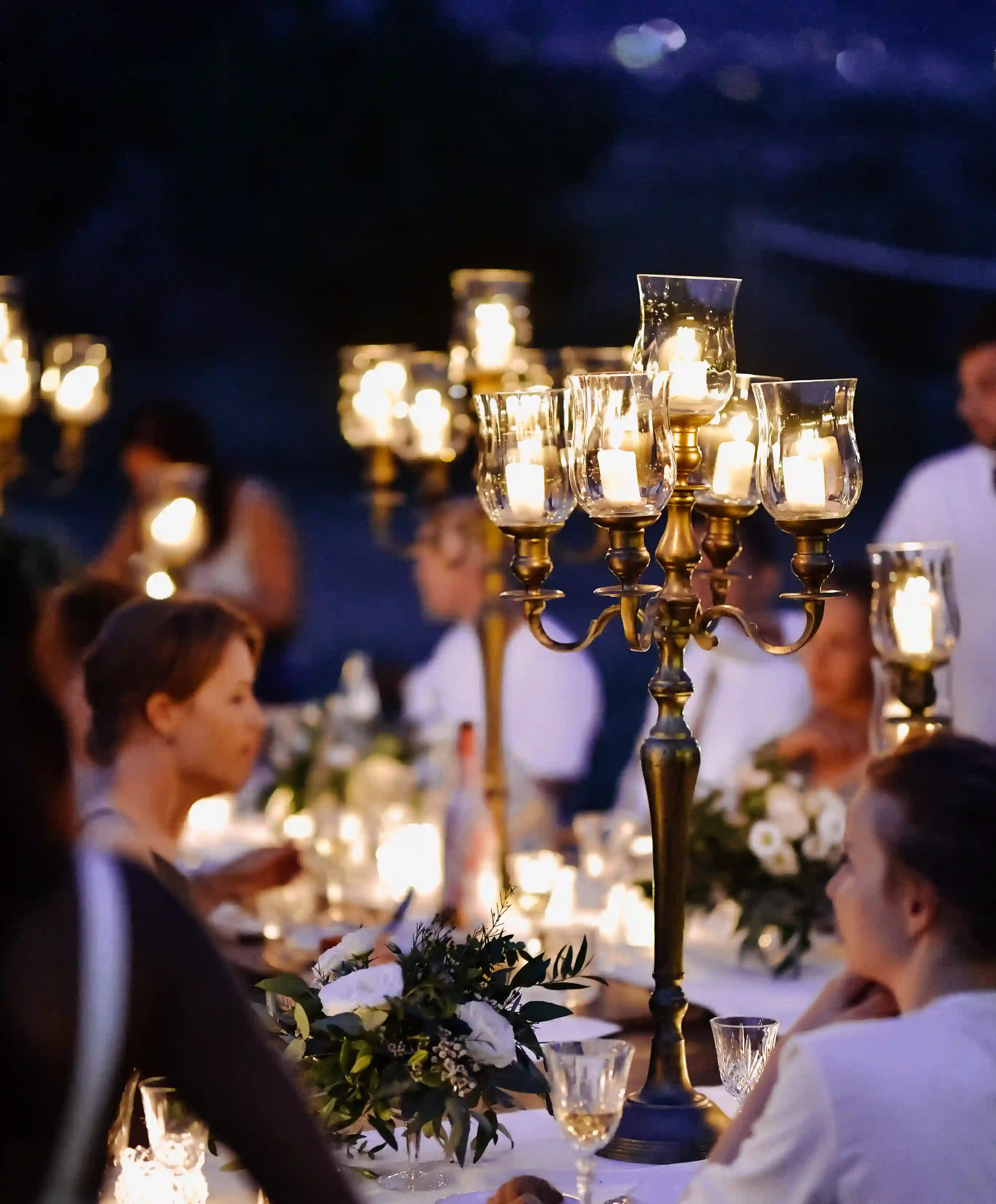 Close-up of an ornate gold candelabra with lit candles and white flowers on a dining table at an evening event