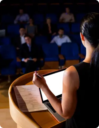 Woman standing at a podium giving a presentation to an audience in a dark hall